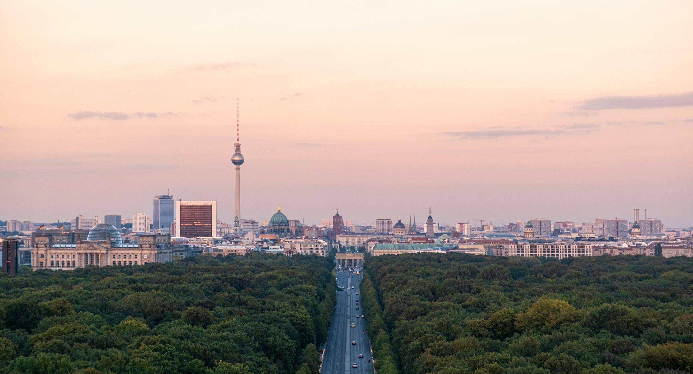 A wide aerial view of Berlin at dusk, the city flat to the horizon with the television tower rising from it.
