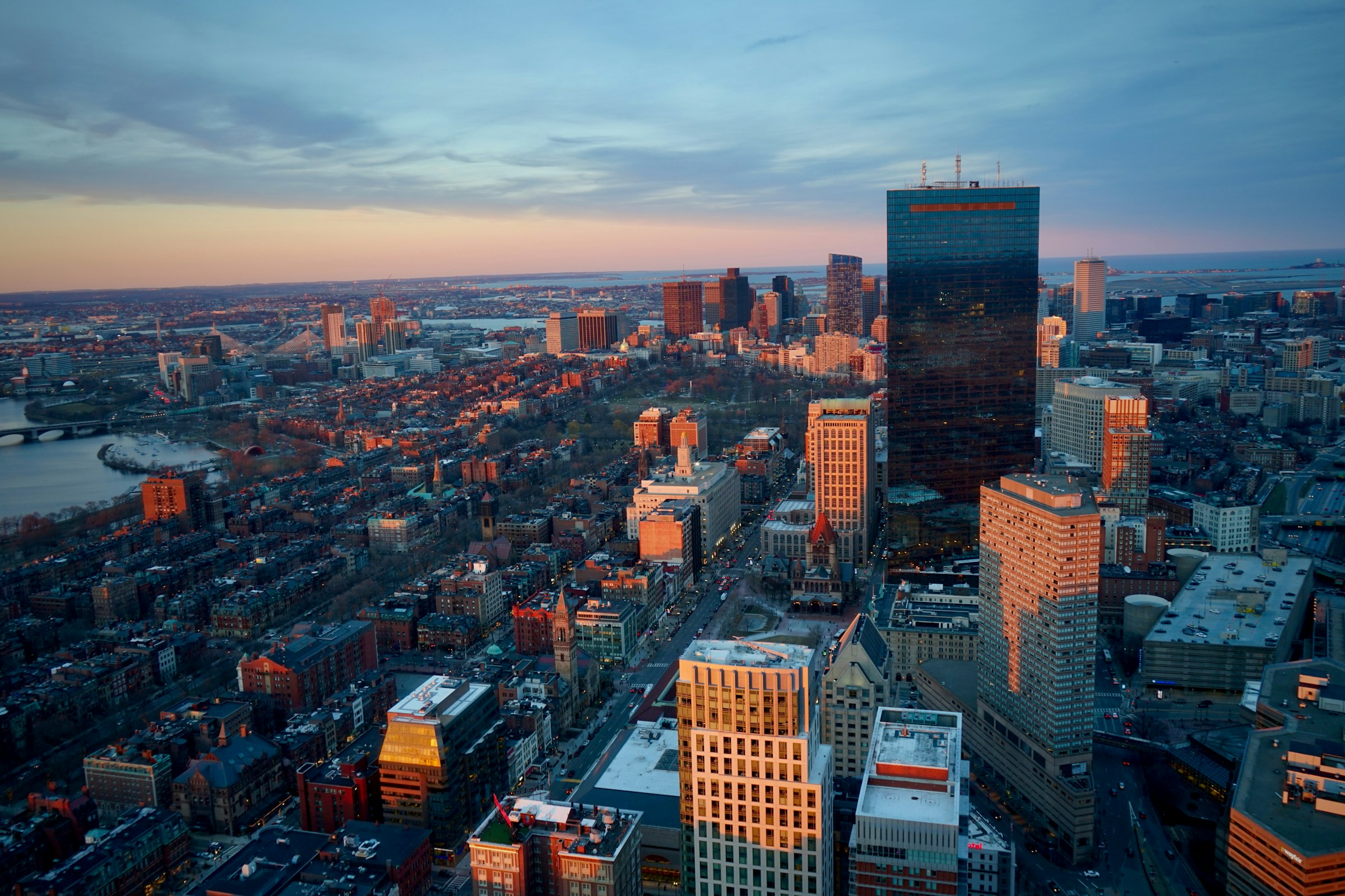 An aerial view across Boston at sunset, the towers of the Back Bay catching the low light.