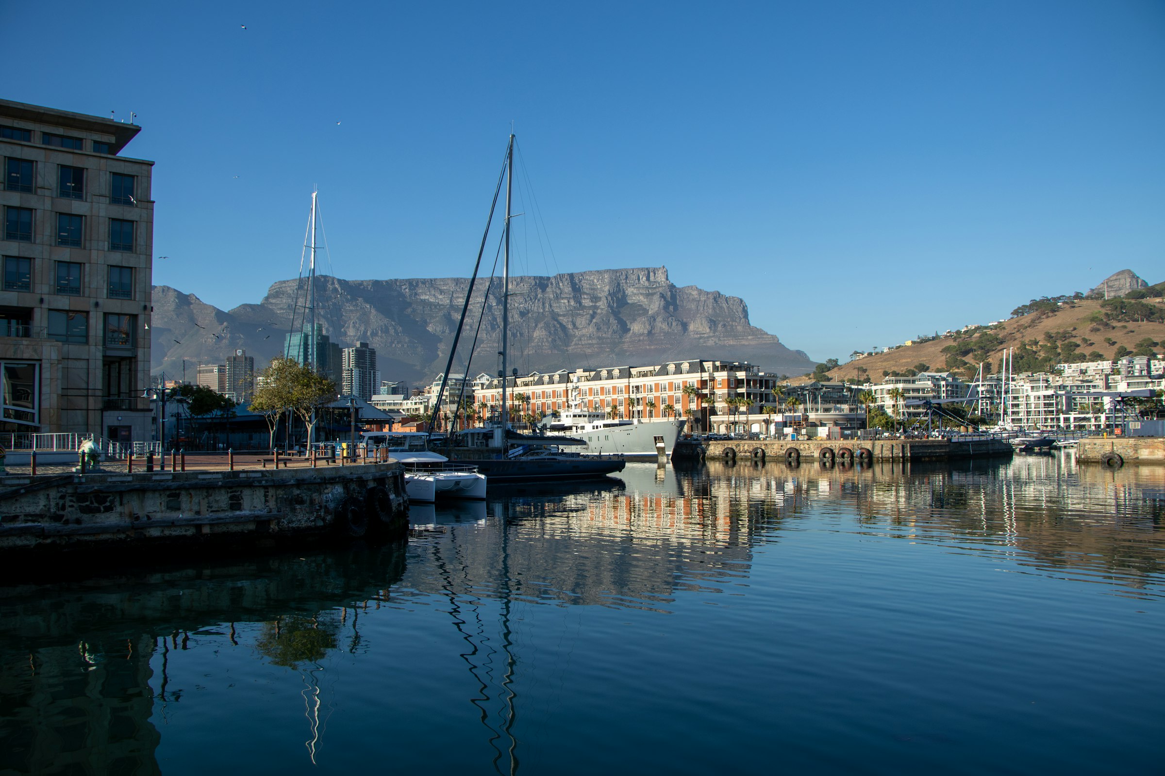 Moored yachts in the calm water of the V&A Waterfront, with Table Mountain beyond the buildings.