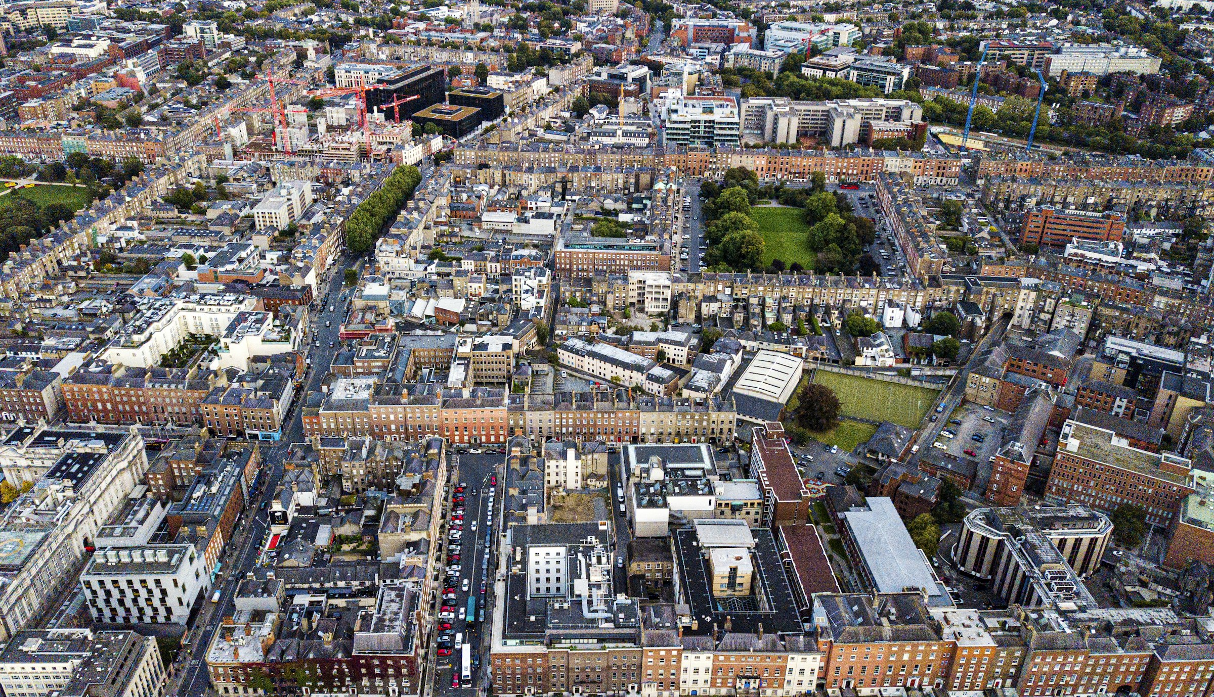 An aerial view over terraces of red-brick Georgian houses and a green square in central Dublin.