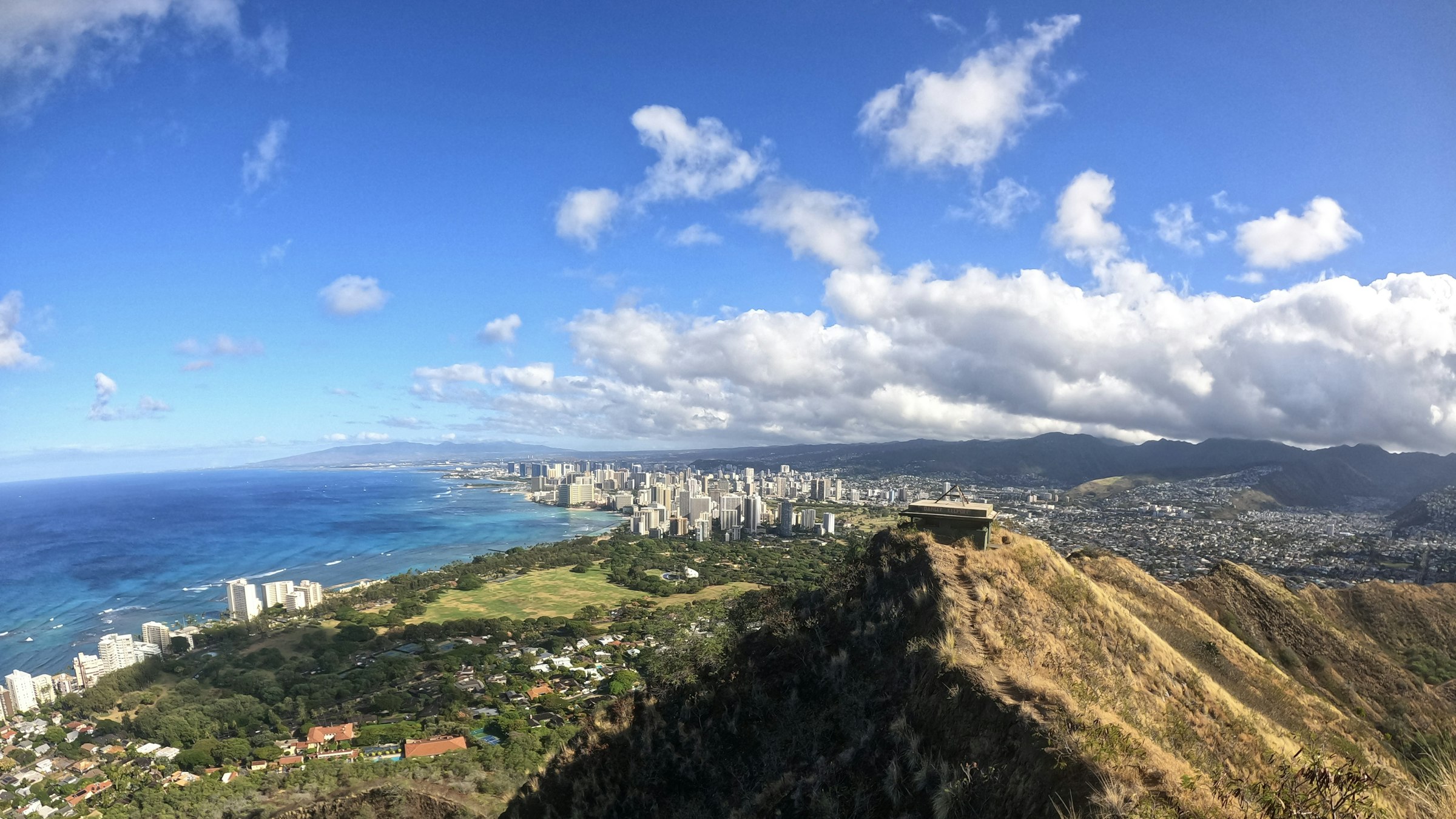 The grassy ridge of Diamond Head crater, with Waikiki's towers and the ocean in the distance.