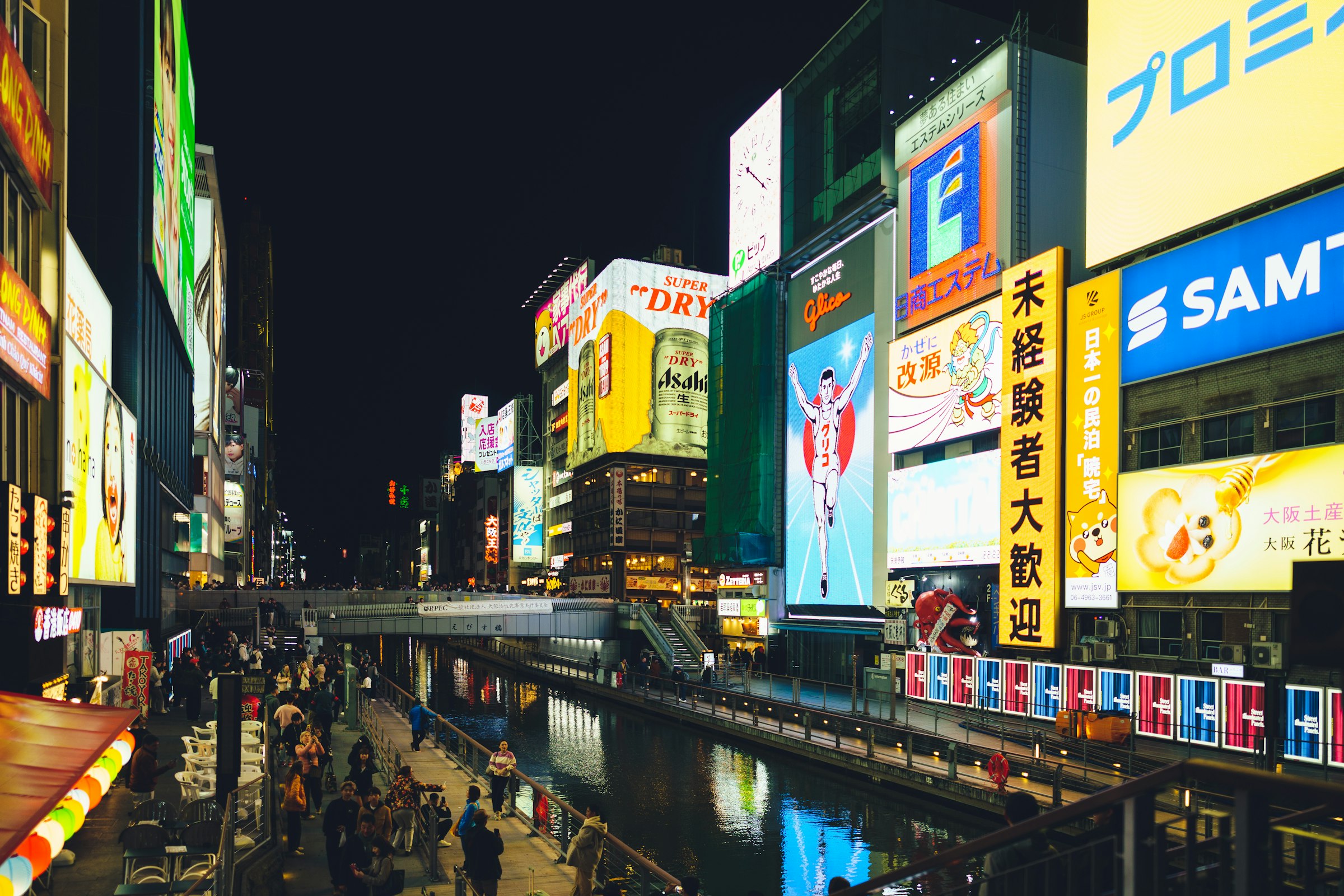 A canal lined with bright neon advertising signs and crowds on the walkways at night.