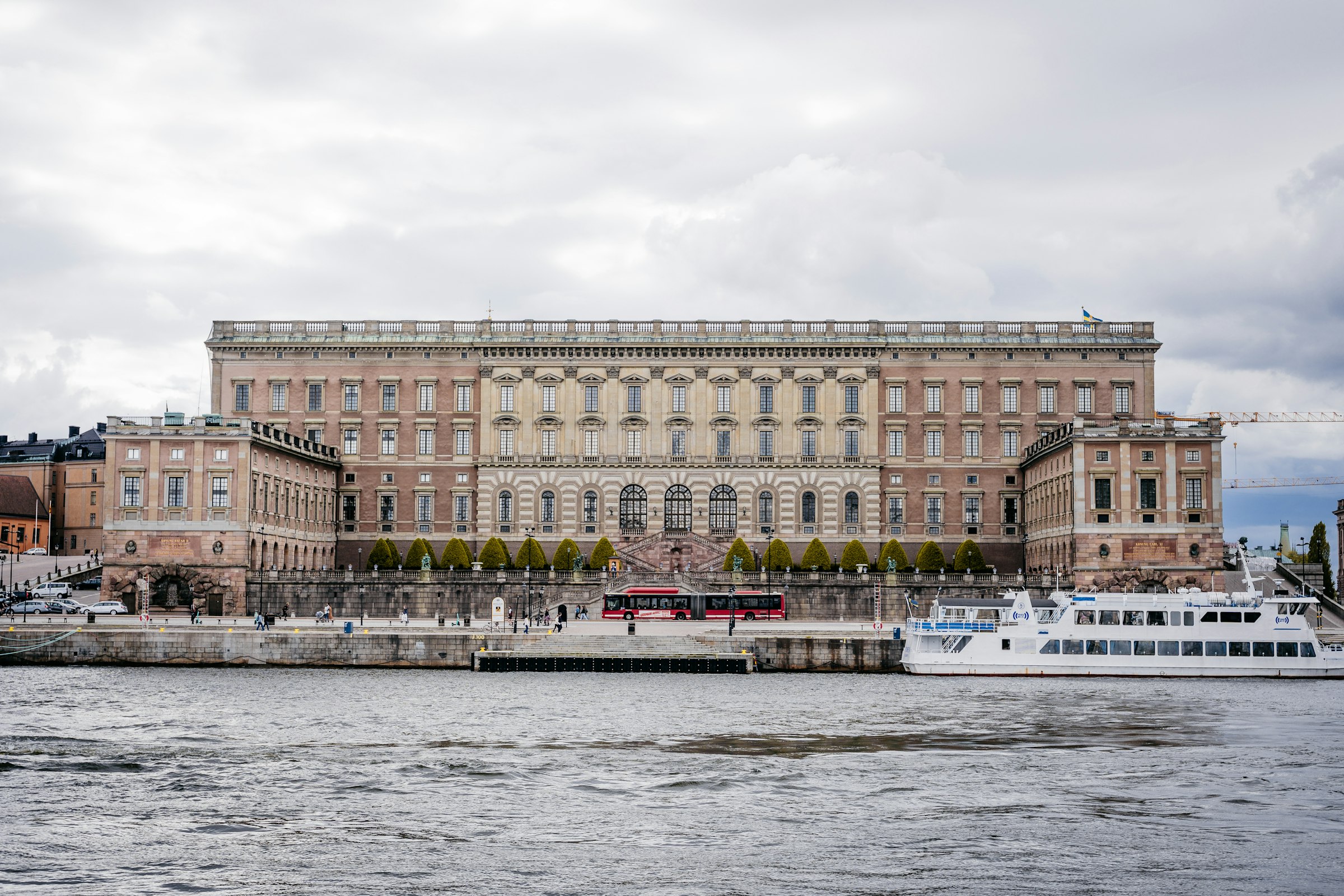 The long stone front of Stockholm's Royal Palace above a quay, with white ferries moored below.