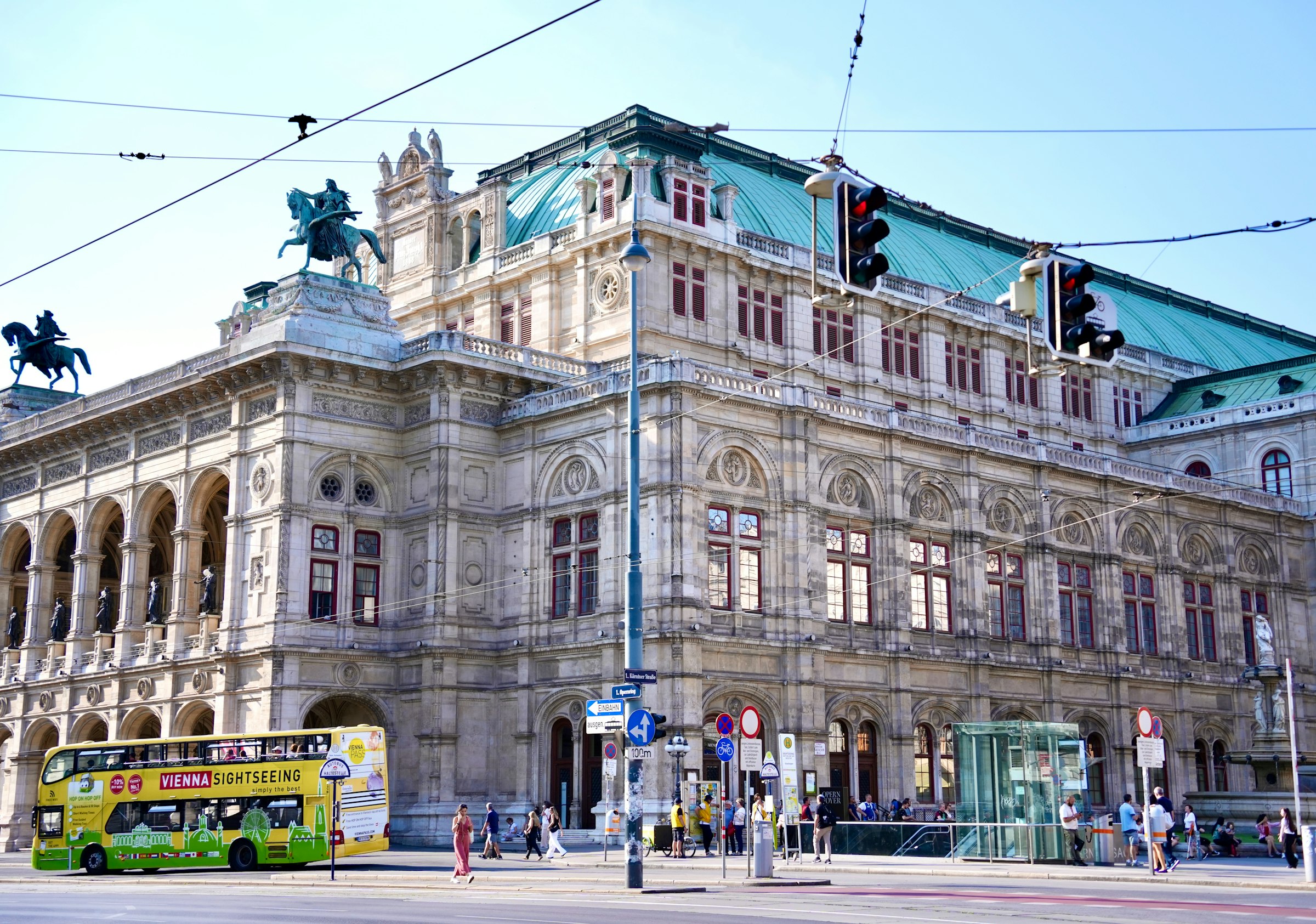 Vienna's state opera house, a stone building with green copper roofs, with a tram line and traffic lights in front.